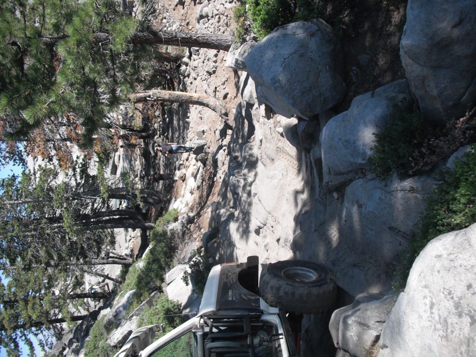 White off-road vehicle with exposed roll cage on a steep, rocky trail