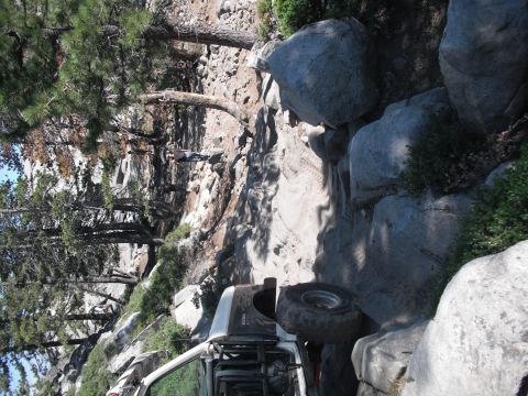 1991 Ford Bronco - A vehicle navigates a challenging rocky terrain, with trees and boulders lining the path.