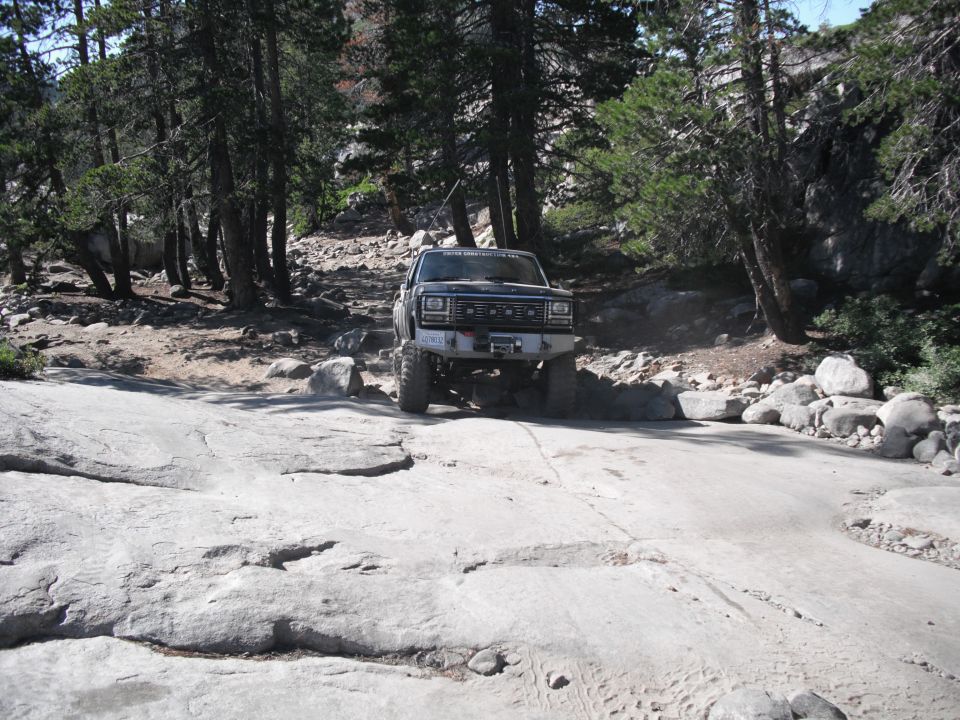 Off-road truck on rocky trail, trees and boulders around