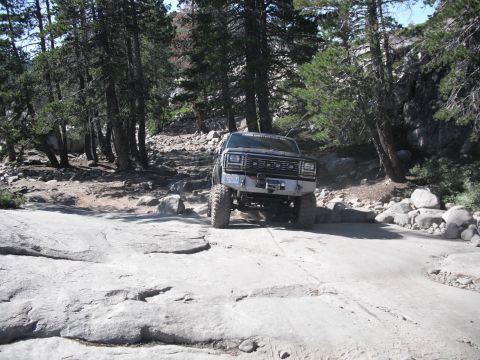 1991 Ford Bronco - A lifted, dark-colored SUV navigates a challenging rocky trail, suggesting off-road capability.