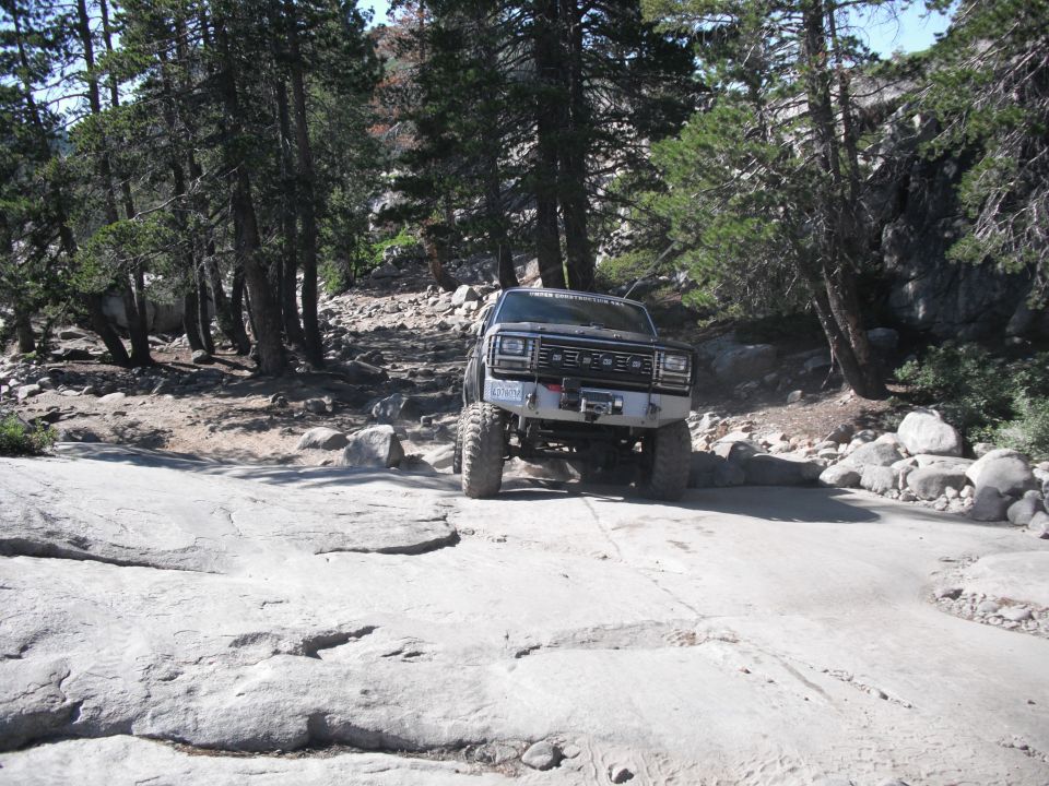 Front view of a lifted, dark-colored 1980s SUV with a winch on a rocky trail