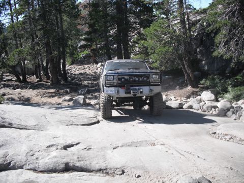 1991 Ford Bronco - Ford Bronco navigates a challenging off-road trail with large rocks and trees.