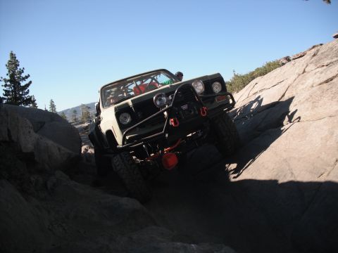 1991 Ford Bronco - An off-road vehicle tackles a challenging rocky incline under a clear blue sky.