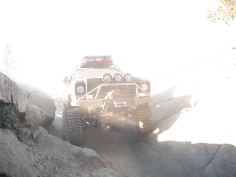 1991 Ford Bronco - An off-road SUV navigates a challenging rocky trail, kicking up dust.