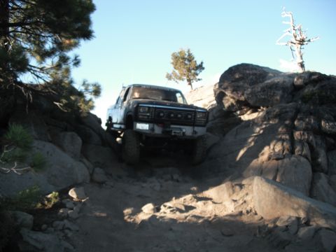 1991 Ford Bronco - A black Ford Bronco navigates a challenging rocky terrain under a clear blue sky.