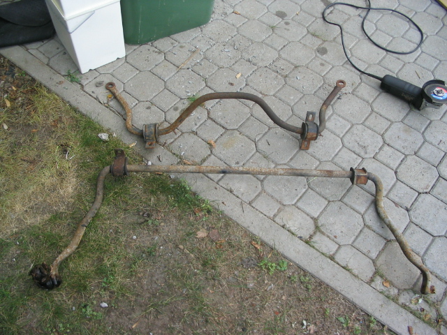 Two rusty sway bars laid out on a paved surface next to an angle grinder