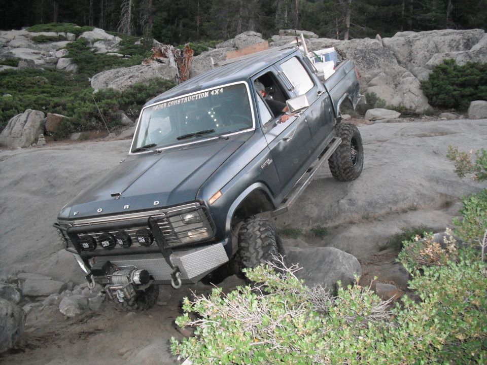 Blue Ford F-Series pickup truck with off-road modifications navigating rocky terrain