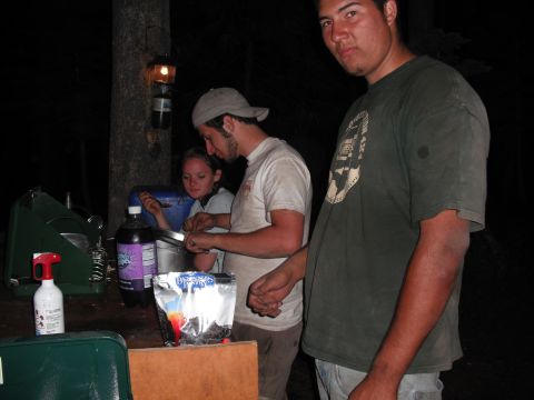 1991 Ford Bronco - People are cooking food outdoors at night, with a camping stove and supplies on a table.