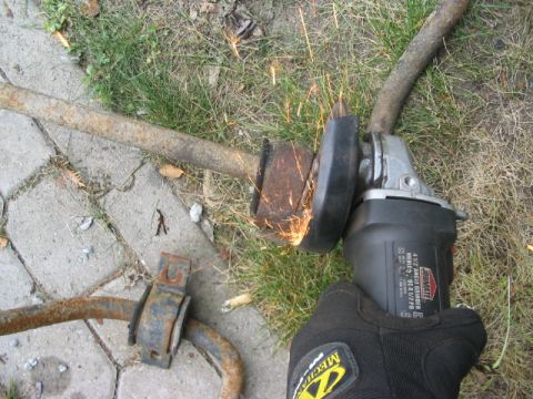 1986 Ford Bronco - An angle grinder is used to cut a rusty sway bar, with sparks flying from the cutting action.