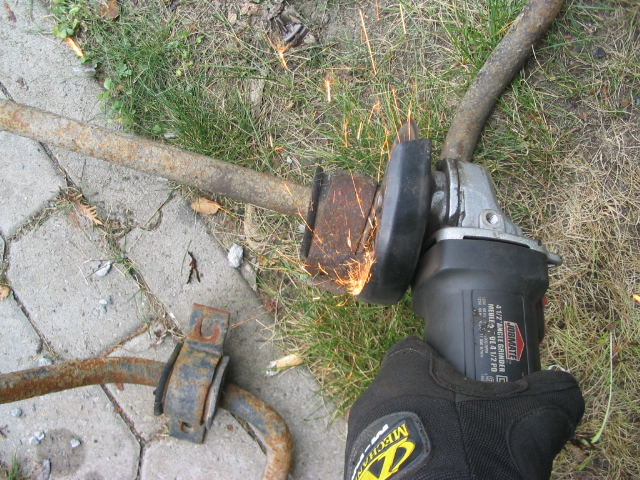Grinding sparks fly as an angle grinder cuts through a rusty sway bar mounted on the ground