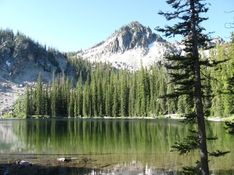 1981 Ford Bronco - Alpine lake scenery with a granite peak rising above a dense conifer forest, the treeline mirrored in still green water. No vehicle or vehi…