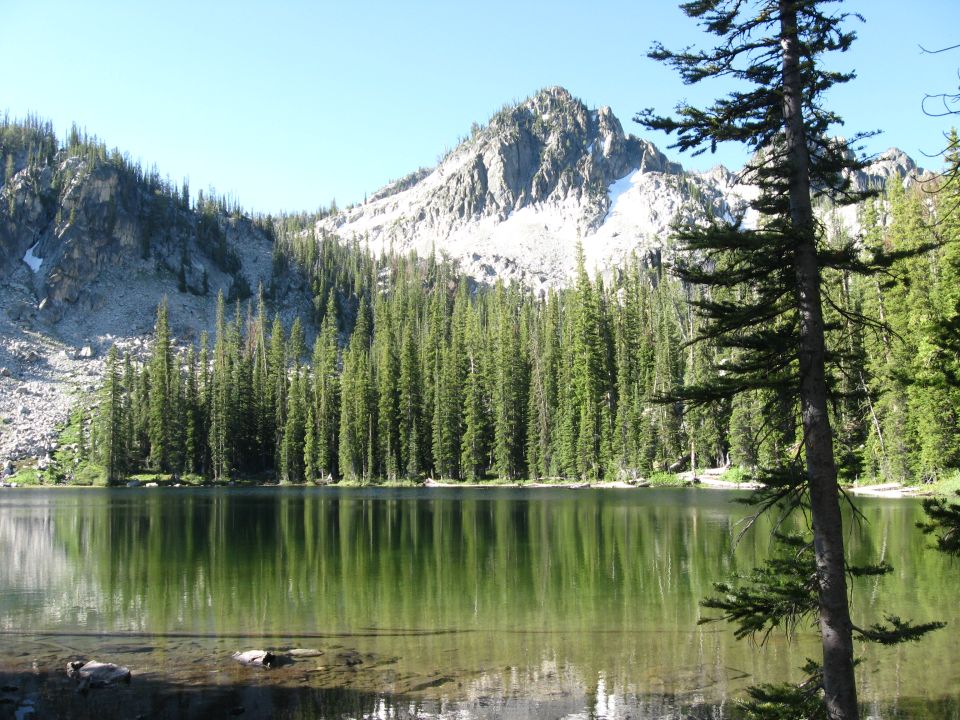 Alpine lake with granite peak and conifer forest reflected in still water