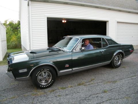 1968 Mercury Cougar - A man sits behind the wheel of a classic coupe parked in front of a garage.