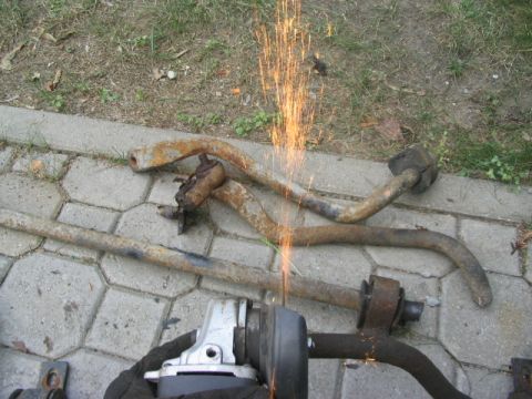 1986 Ford Bronco - An angle grinder cuts through rusty suspension parts on a paved surface, with sparks flying.