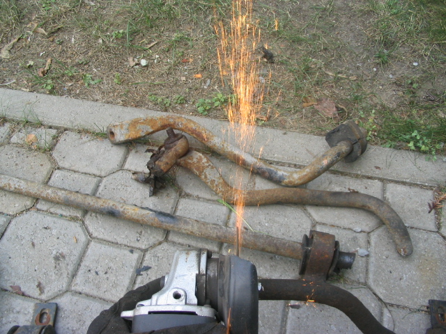 Rusty metal suspension parts being cut by an angle grinder on a paved surface