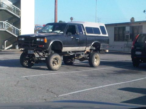 1986 Ford Bronco - This lifted pickup truck, equipped with a camper shell, is parked in a lot. The registry claims it is a 1986 Ford Bronco, but it does not m…