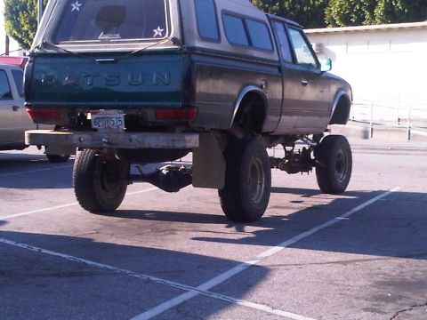 1986 Ford Bronco - This lifted Datsun pickup truck has a camper shell and a custom bumper. The license plate is visible.