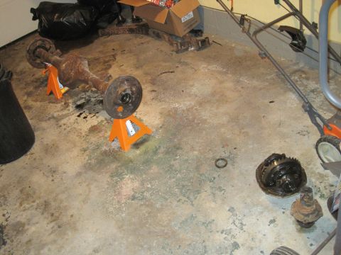 1979 Ford Bronco - A disassembled differential and axle assembly rests on jack stands in a garage.