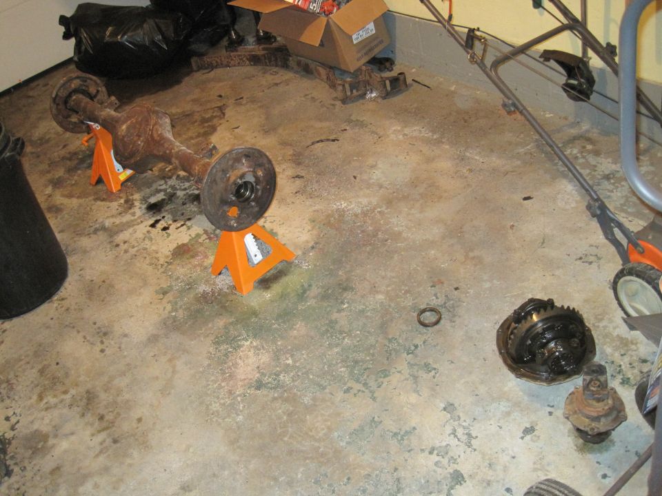 Rusty differential and axle assembly on orange jack stands, with a differential housing on the floor