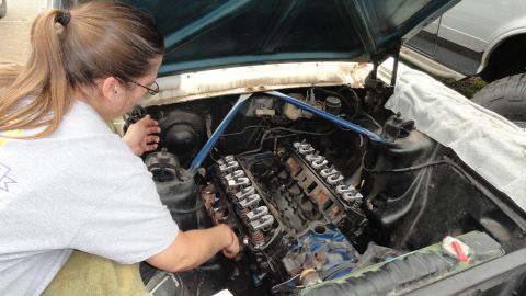 1964 Ford Fairlane - A person works on the V8 engine of a car, with the hood open.