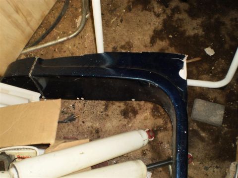 1978 Ford Bronco - A damaged dark blue fender flare lies on the floor amidst other parts and debris.