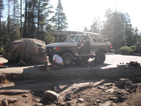 1991 Ford Bronco - People work on the front of a 1991 Ford Bronco parked on a rocky surface, with a canoe secured to its roof rack.