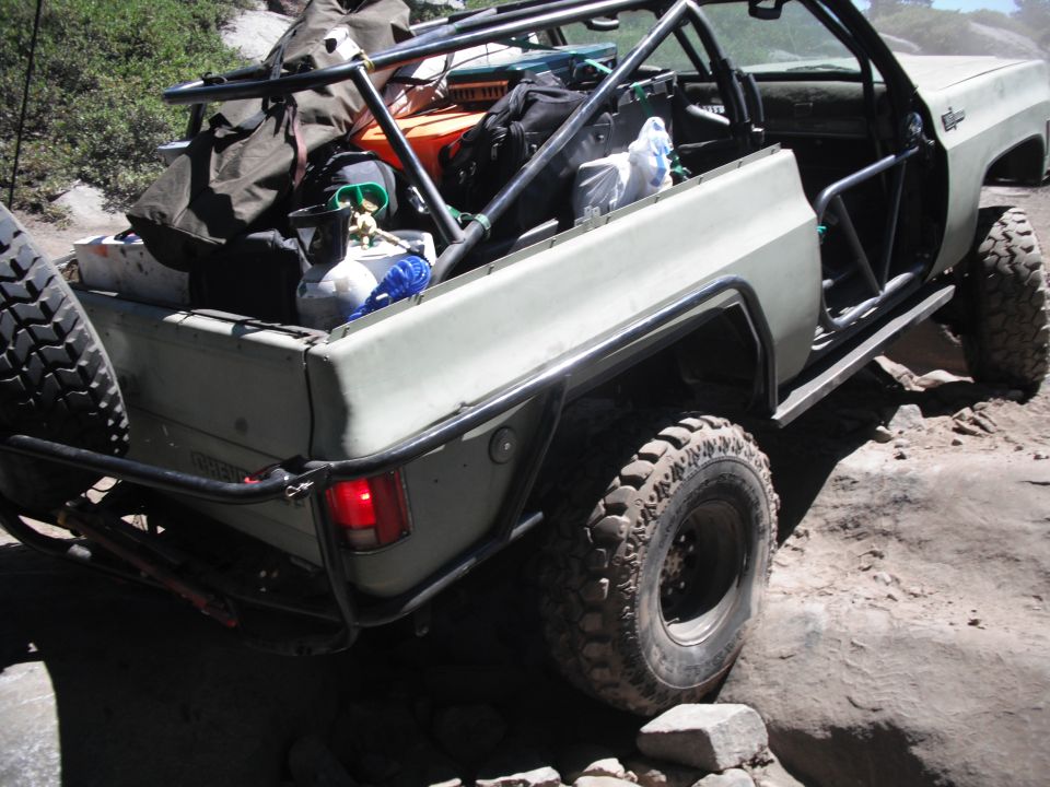 Olive green off-road vehicle with roll cage and cargo in bed, seen from rear-right