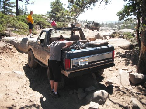 1991 Ford Bronco - A man loads gear into a Ford Bronco as another vehicle is seen in the background on a rocky trail.