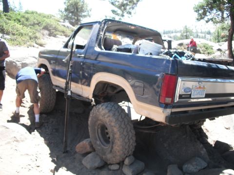1991 Ford Bronco - A blue 1991 Ford Bronco navigates a challenging rocky trail, with a person attending to the front wheel.