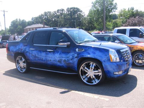 2001 Chevrolet Silverado 1500 - A custom-painted Cadillac Escalade EXT is parked in a lot, its unique blue flame design and large chrome wheels.