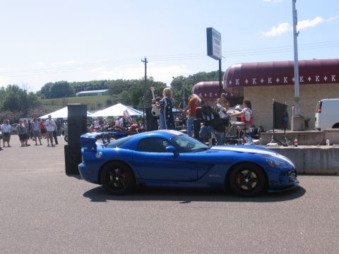2001 Chevrolet Silverado 1500 - A blue sports car with white racing stripes is parked in front of a band performing at an outdoor event.