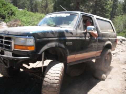 1991 Ford Bronco - This lifted Ford Bronco navigates a challenging, rocky terrain with its driver visible through the window.