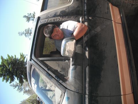 1991 Ford Bronco - A man rests his arm out the window of a dark-colored SUV, with trees and a bright blue sky in the background.
