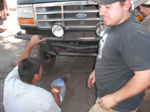 1991 Ford Bronco - Two men are working on the front bumper and grille of a dark-colored Ford truck.
