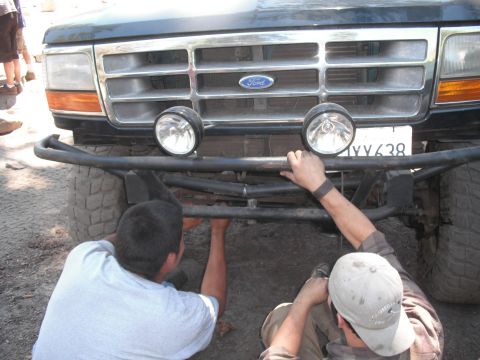 1991 Ford Bronco - Two men are working on the front bumper of a dark blue Ford truck.