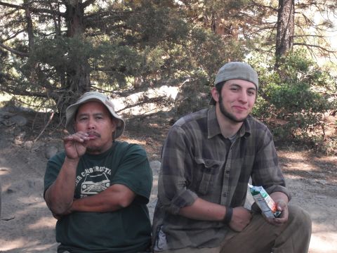 1991 Ford Bronco - Two men relax outdoors under trees, one smoking and the other holding a juice box.