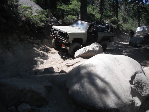 1991 Ford Bronco - An off-road vehicle tackles a challenging rocky path, with another vehicle visible further down the trail.