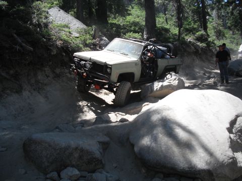 1991 Ford Bronco - A modified off-road vehicle navigates a challenging rocky trail in a wooded area.