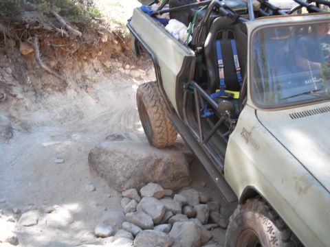 1991 Ford Bronco - An off-road vehicle navigates a rocky trail with its doors removed and a roll cage installed.