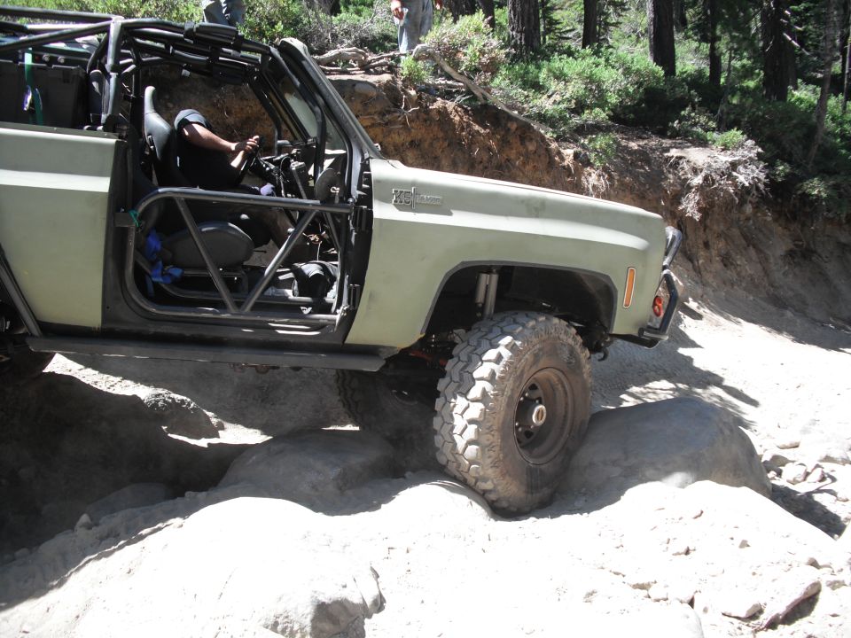 Olive green off-road vehicle with roll cage navigating a rocky trail