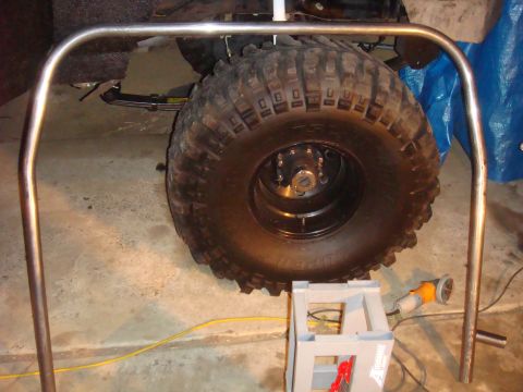 1992 Ford Bronco - A roll cage frame is positioned over a large off-road tire, with a grinder visible in the background.