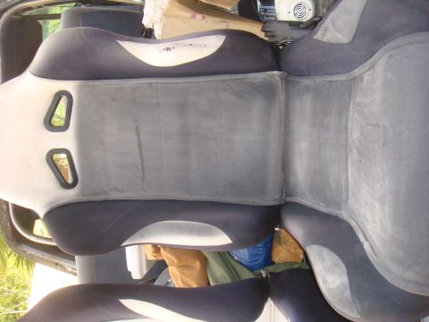 1992 Ford Bronco - The interior of a vehicle shows dark seats with light grey accents and some items stored behind them.