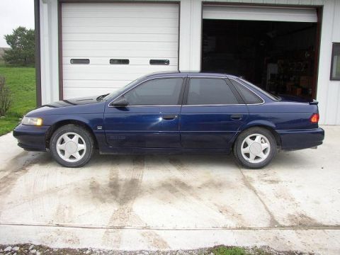 1993 Ford Taurus - Side view of a dark blue sedan parked in front of a garage door.