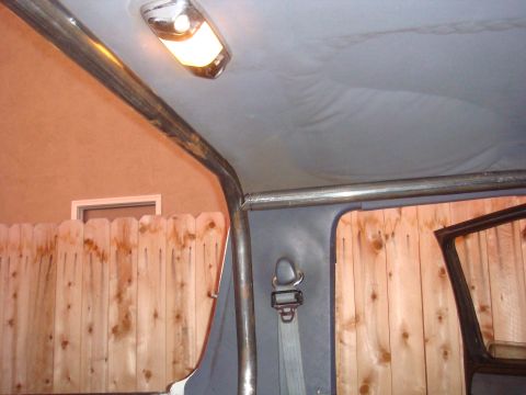 1992 Ford Bronco - The interior of a vehicle shows a roll cage and a seatbelt, with a wooden fence visible through the window.