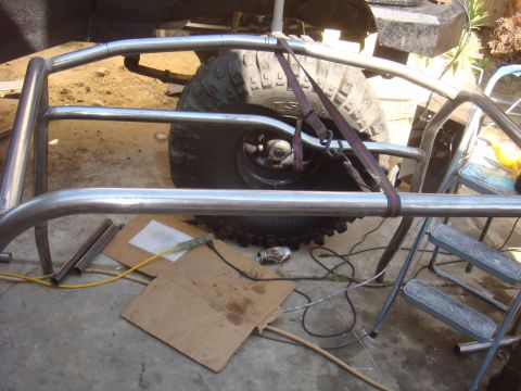1992 Ford Bronco - A custom roll cage is being fitted around a large off-road tire, with various tools and materials scattered on the ground.