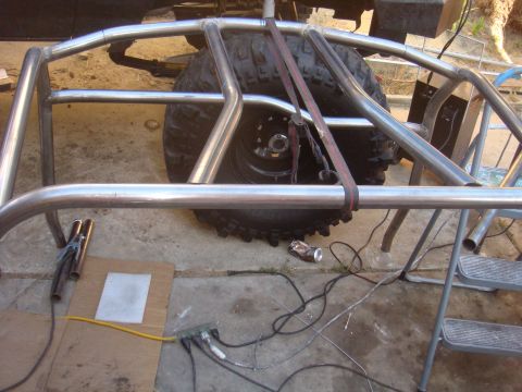 1992 Ford Bronco - A custom roll cage is installed over the spare tire of an off-road vehicle, with welding equipment nearby.