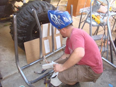 1992 Ford Bronco - A person is welding a custom roll cage structure next to a large off-road tire.