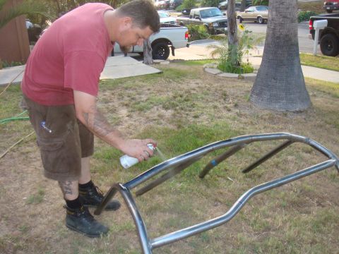 1992 Ford Bronco - A man sprays a metal roll cage with white paint outdoors.