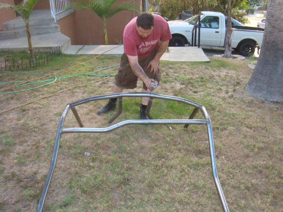 Man spraying a metal roll cage with a can of spray paint outdoors