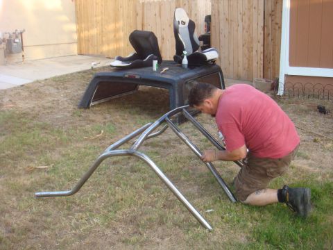 1992 Ford Bronco - A man fabricates a roll cage in a grassy yard, with a truck cap and racing seats nearby.